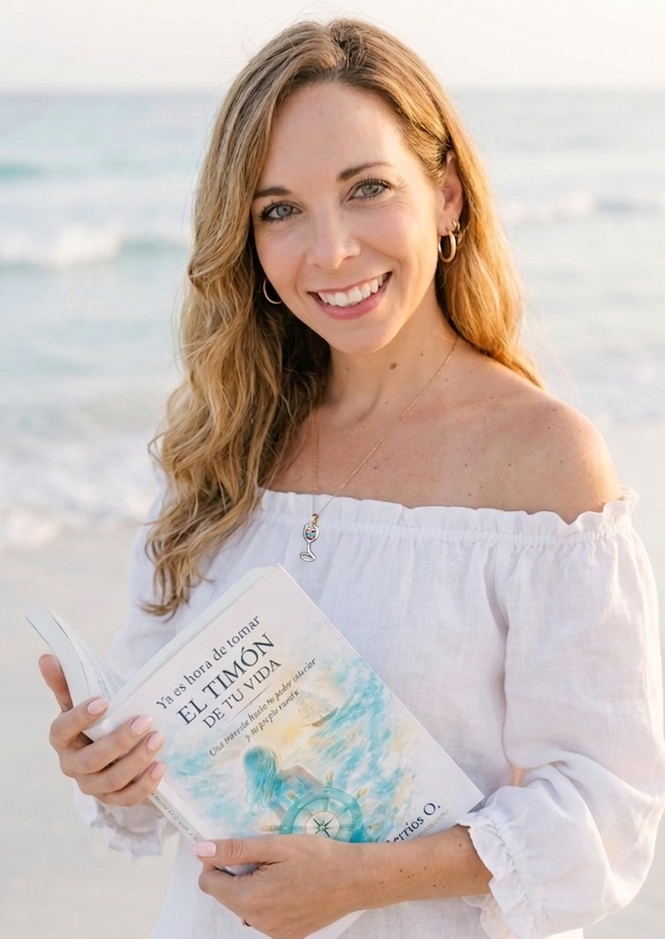 Brenda Berríos O. sosteniendo su libro "Ya es hora de tomar el timón de tu vida" frente al mar.